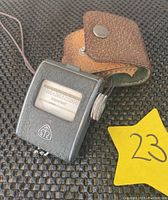 Front view of the Metra Blansko Exposimet light meter showing the exposure scale, adjustment dial, and brand logo along with the leather carrying case.