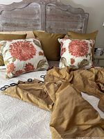 Two large gold drapes with black rings laid on bed with matching solid gold pillows and two floral pillows in front