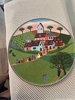 Top view of Villeroy & Boch Naïf Laplau cake plate showing detailed colorful village scene design with people, trees, and houses.