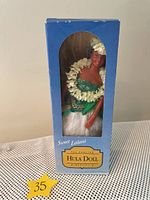 Front view of Sweet Leilani My Hawaii Hula Girl dancer doll in original blue box with window showing the doll wearing a green top, white skirt, and floral lei.