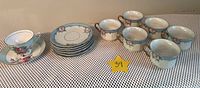 Complete set of 6 tea cups and 6 matching saucers with floral designs laid out on a table with a star tag showing lot number.