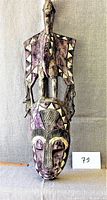Front view of the entire carved wooden African mask showing detailed geometric painted patterns and copper side ornaments.