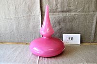 Front view of handmade pink glass vase with tall thin neck and wide round base on neutral fabric background.