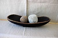 Elongated mango wood bowl holding two beaded balls—one natural wood bead and one white bead ball displayed on light fabric background.