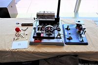 Full view of the Wilesco model steam engine and the separate work station with several tools and parts laid out on a beige cloth