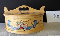 Side view of bentwood box showing painted floral design and wooden fastener lid closure