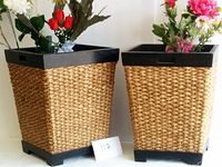 Pair of square wooden planters with woven grass exterior, black rim on top and bottom, with artificial flowers inside for display only