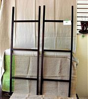 Front view of two dark wood towel ladders standing upright against a fabric backdrop.