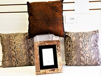 Three cushions and one picture frame displayed together on a white background against slatwall, showing the solid brown cushion on top and two snake skin patterned cushions below, with the picture frame centered in front.