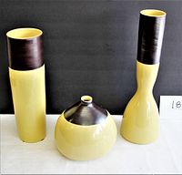 Three yellow and brown ceramic vases against black backdrop with white surface