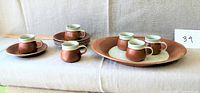 Six cups and saucers with an oval tray arranged on a beige fabric background. The cups have brown outer glaze and white inner glaze, while saucers and tray also share the brown tone.