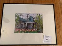 Framed art print showing a stone house with a curved wrap-around porch, surrounded by tulips and trees.