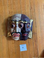 Front view of two-faced Asian mask showing detailed painted features and gold accents