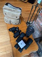 Overview of three binoculars, beige carrying case, and fireplace tools on wooden table