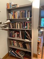 Photo showing a six-shelf grey bookshelf containing various books organized but not alphabetically or by size. The books are hardcover and paperback varying from literature to science topics.