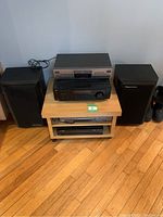 Full view of entertainment electronics system on wooden rolling console including speakers, JVC stereo receiver and player components.