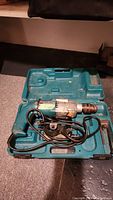 Makita power drill inside teal molded carrying case with power cord placed inside case.