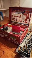 Overview of Milwaukee 12 Volt cordless driver/drill kit in open red metal case with accessories and detailed instructions on lid.