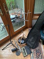 Photo showing guitar case, foldable music stand, microphone stand, microphone in case, basket with cables.