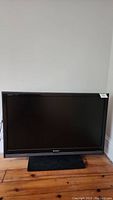 Full front view of Sharp Aquos TV, 42 inch flat screen, black frame on a wooden floor.