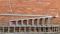 Full side view of the metal smaller ladder leaning against a brick wall with visible steps and metallic frame.