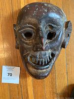 Top-down photo of the carved dark wooden mask showing facial features and a lot tag alongside