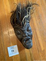 Front view of wood carved mask with dark coarse hair attached at top.