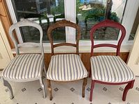 Front view of three antique dining chairs, white, natural wood, and red painted finishes, with striped seat cushions