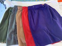 Photo showing five skirts laid out side by side in colors olive green, dark gray, tan, red, and purple.