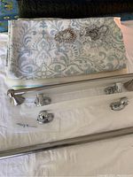 Folded patterned fabric shower curtain, two metal shelves, chrome curtain rod and hardware pieces including hooks and towel rack mounts on a flat surface.