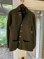 Full view of the long felted wool jacket showing sage green body, black edging, metal buttons, and pockets.