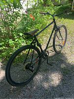 Photo of the black 7-speed bicycle with brown seat outdoors, showing rear and side view with gear cassette and reflectors.
