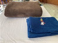 Brown fleece blanket and blue Christmas-themed fleece blanket on table showing size and visual details