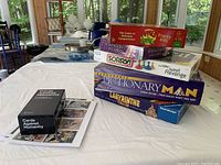 Overview photo showing the stacked boxed games including Apples to Apples, Hits & Misses Party Hunt, Sorry, Sweet Revenge, Pictionary Man, Labyrinth Master, and Cards Against Humanity alongside some game pieces.