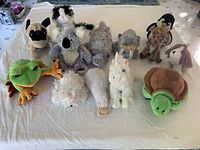 Overview of all 12 plush stuffed animals laid out on a white sheet showing various animal types and colors.