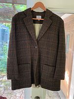 Brown Irish wool gingham blazer hanging on wooden hanger in front of glass door, showing full front and sleeves, highlighting gingham pattern and two front patch pockets.