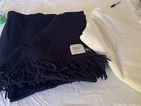 Folded navy blue Nido Notte pure wool throw with label visible and part of white IKEA Polarvide blanket showing under it