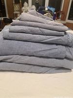 Folded stack of denim-colored cotton bedding showing sheets and pillowcases neatly layered.