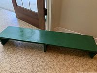 Green wooden shoe rack placed on floor showing full length and condition