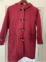 Child's raspberry wool pea coat with four wooden toggle buttons, size 10, hanging on a hanger.