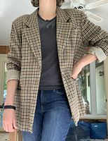Model wearing light brown and green check wool blazer, sleeves rolled up, paired with jeans