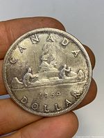 Photo of the reverse side of the 1959 Canadian silver dollar coin showing the Voyageur design with two men paddling a canoe and inscription of denomination and year.