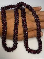 Photo of antique braided garnet necklace laid over a hand showing the rich deep red garnet beads tightly clustered and braided into a continuous strand.