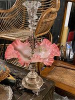 Full view of cranberry glass bowl with ruffled edges and floral/gold decoration on silver-plated base with clear glass vase.