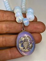 Close-up of the silver pendant with grapevine design on a moonstone base, held between fingers showing bead size and detail.