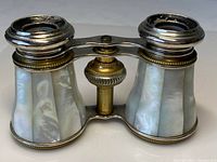 Front view of antique opera glasses showing trapezoidal mother of pearl panels and metal frame.