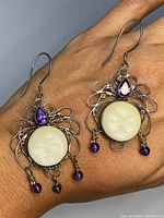 Front view of antique silver earrings on hand showing carved moon face, amethyst stones, and dangling beads.