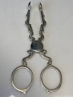 View of full silver tongs showing wavy engraved arms and circular finger loops