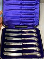 Full view of six antique solid silver butter knives in original fitted display box with blue velvet and silk lining.