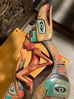 Front-quarter view of the entire wooden rattle, handle visible at bottom, shows human figure and creature body